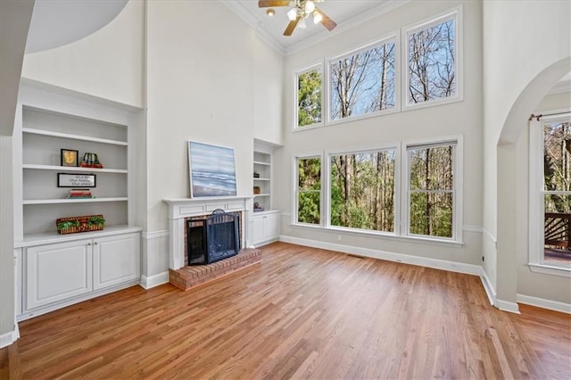 unfurnished living room featuring light wood finished floors, built in shelves, a brick fireplace, crown molding, and baseboards