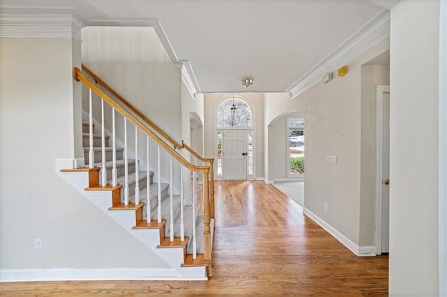 foyer with wood finished floors, baseboards, arched walkways, stairs, and crown molding