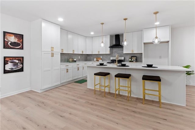 kitchen featuring white cabinetry, wall chimney exhaust hood, a kitchen island with sink, and light hardwood / wood-style flooring