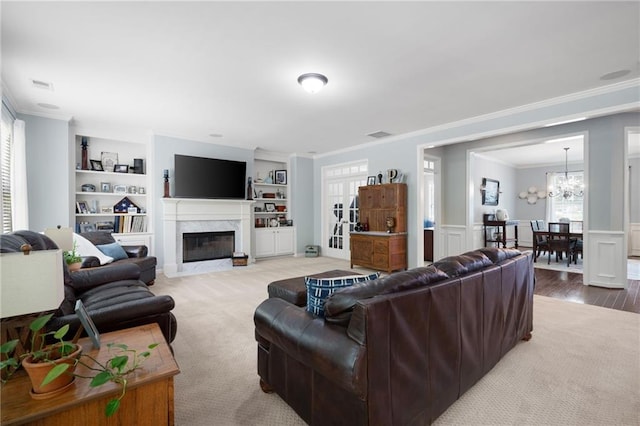 living room featuring crown molding, built in shelves, a fireplace, carpet floors, and a notable chandelier