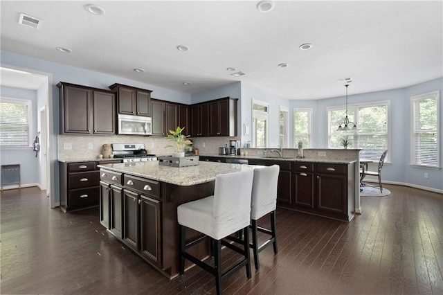 kitchen with dark wood-type flooring, pendant lighting, stainless steel appliances, and a kitchen island