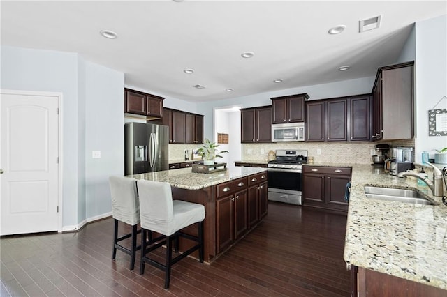 kitchen featuring appliances with stainless steel finishes, sink, a kitchen island, dark wood-type flooring, and light stone counters