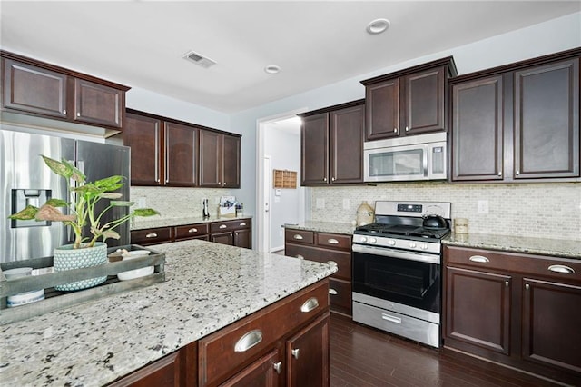 kitchen with dark brown cabinetry, dark wood-type flooring, backsplash, stainless steel appliances, and light stone counters