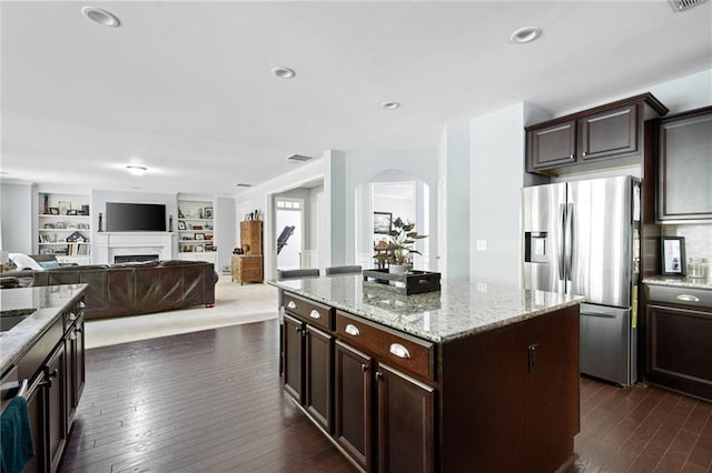 kitchen featuring stainless steel fridge with ice dispenser, a kitchen island, dark brown cabinetry, built in features, and light stone counters