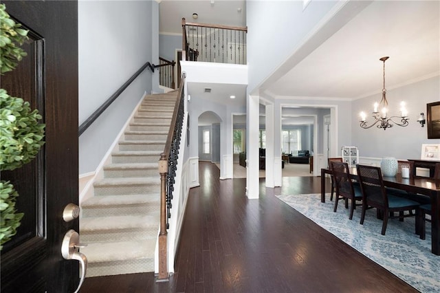 entrance foyer with crown molding, dark wood-type flooring, a high ceiling, and an inviting chandelier