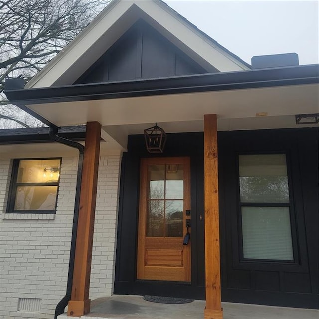 property entrance featuring board and batten siding, brick siding, and covered porch