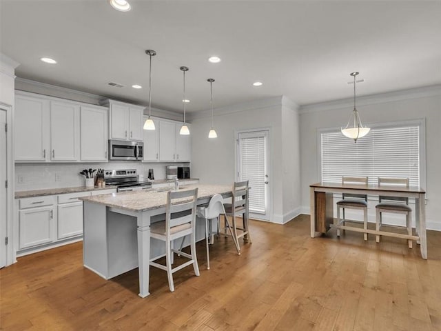 105 Lighthouse Cv SW, Adairsville, GA 30103 - kitchen with stainless steel appliances, a center island with sink, ornamental molding, white cabinetry, and light wood-style flooring