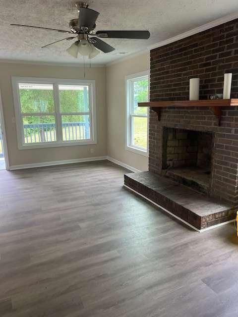 unfurnished living room featuring ceiling fan, a brick fireplace, a textured ceiling, baseboards, and wood finished floors