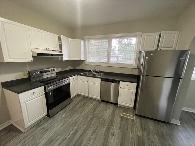 kitchen with dark countertops, appliances with stainless steel finishes, white cabinets, a sink, and under cabinet range hood