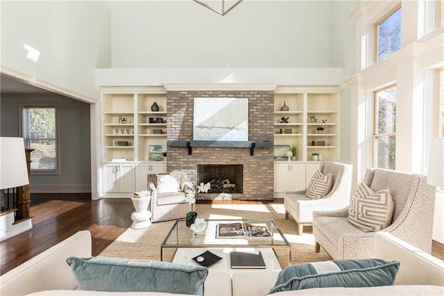 living room featuring dark wood-type flooring, a fireplace, a towering ceiling, and built in shelves