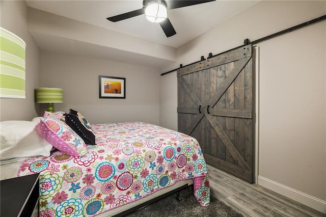 bedroom featuring ceiling fan, a barn door, and hardwood / wood-style floors