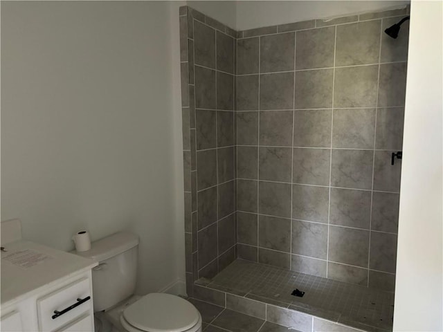 bathroom with vanity, a tile shower, toilet, and tile patterned flooring