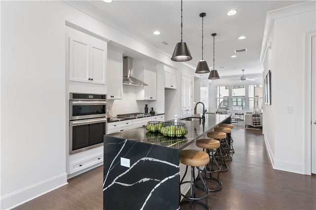 kitchen with a center island with sink, white cabinetry, wall chimney range hood, and dark hardwood / wood-style floors