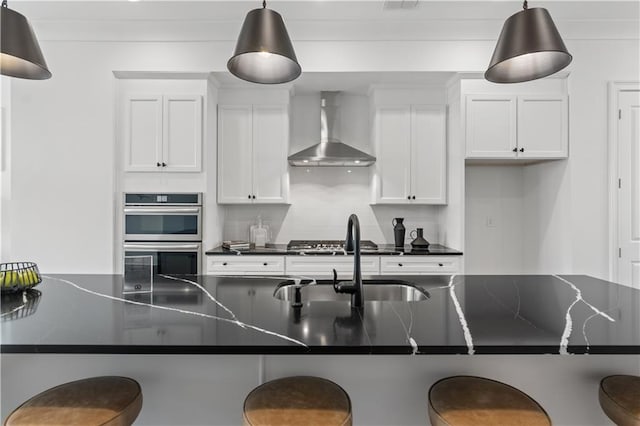 kitchen featuring wall chimney range hood, a kitchen breakfast bar, white cabinetry, double oven, and decorative light fixtures