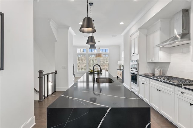 kitchen featuring wall chimney exhaust hood, decorative light fixtures, a kitchen island with sink, and stainless steel appliances