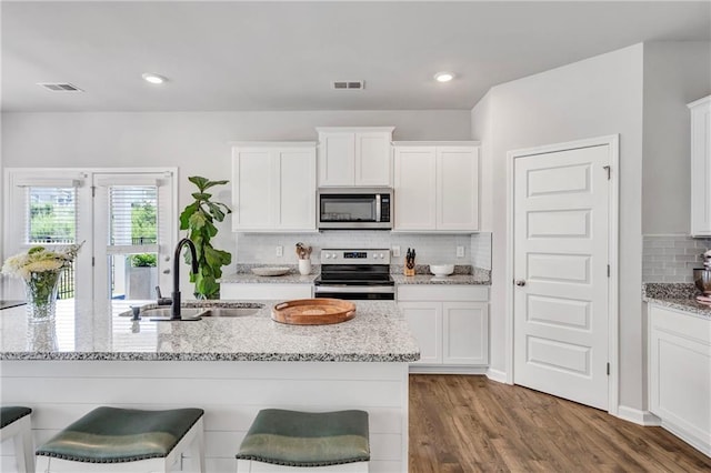 36 Mead Ct, Hoschton, GA 30548 - kitchen featuring stainless steel appliances, decorative backsplash, white cabinets, wood finished floors, and a breakfast bar