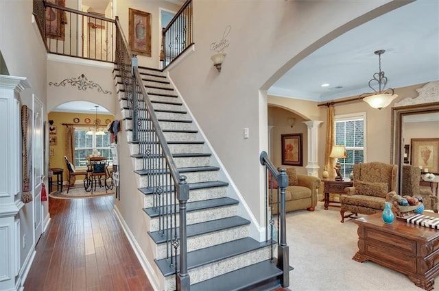 staircase with a notable chandelier, baseboards, decorative columns, arched walkways, and wood-type flooring