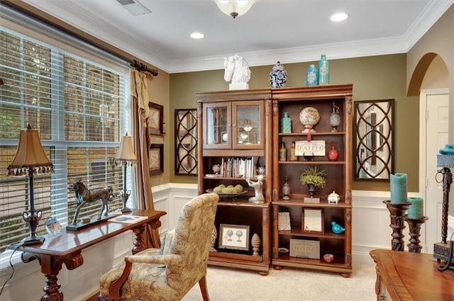 sitting room featuring arched walkways, wainscoting, light colored carpet, and crown molding