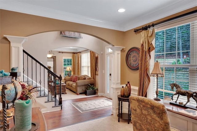 entrance foyer featuring arched walkways, ornamental molding, ornate columns, wood finished floors, and stairs