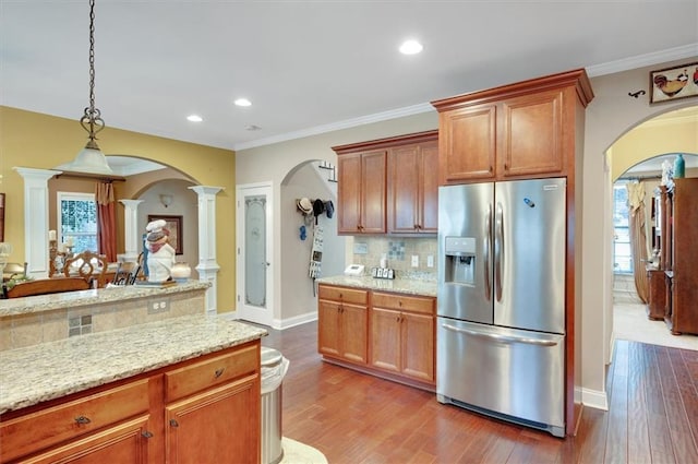 kitchen featuring stainless steel fridge, decorative backsplash, decorative columns, arched walkways, and wood finished floors