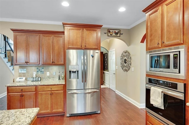 kitchen with arched walkways, baseboards, decorative backsplash, and appliances with stainless steel finishes