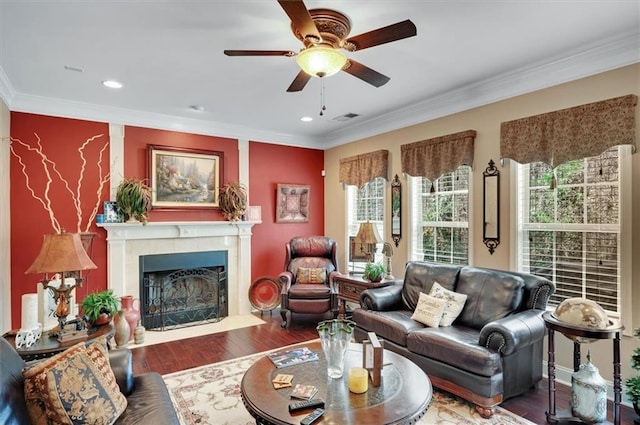 living area with ornamental molding, a fireplace with flush hearth, visible vents, ceiling fan, and wood finished floors