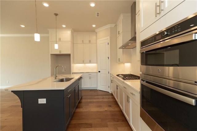 kitchen featuring wall chimney range hood, decorative light fixtures, white cabinets, and a center island with sink