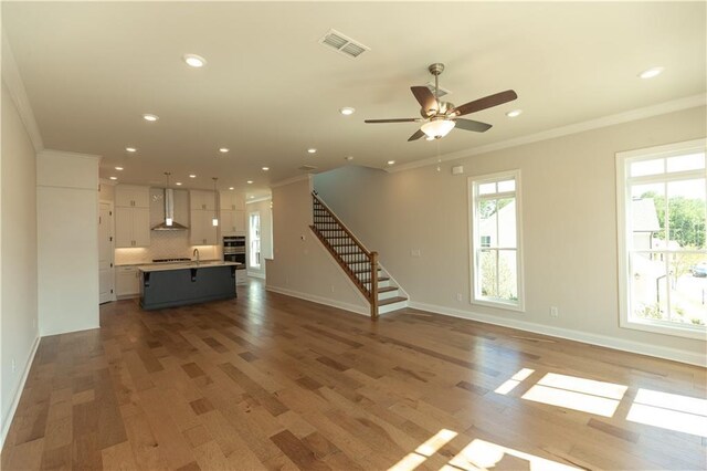 unfurnished living room featuring sink, light wood-type flooring, ceiling fan, and ornamental molding