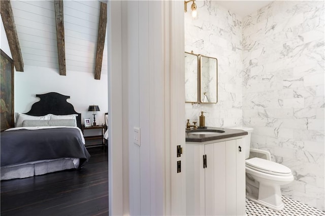 bathroom featuring toilet, lofted ceiling with beams, vanity, wood finished floors, and ensuite bath