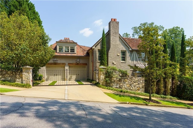 tudor-style house with a garage, a chimney, driveway, and fence