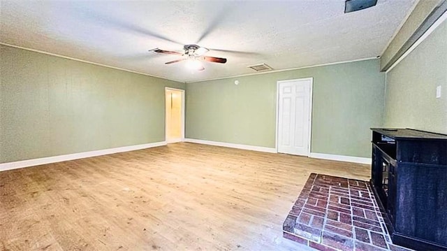 unfurnished living room featuring wood finished floors, visible vents, baseboards, a wood stove, and ceiling fan