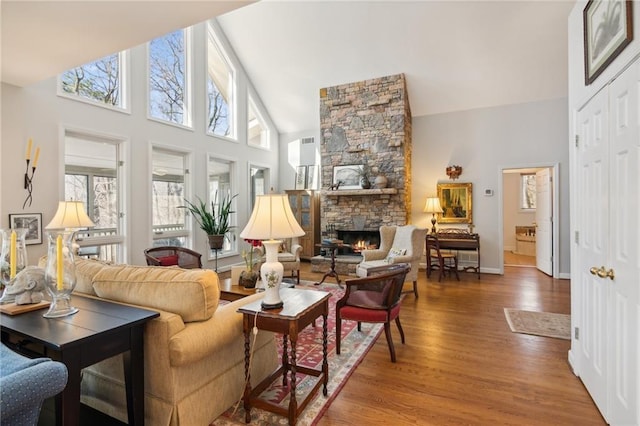 living room featuring hardwood / wood-style floors, high vaulted ceiling, and a stone fireplace