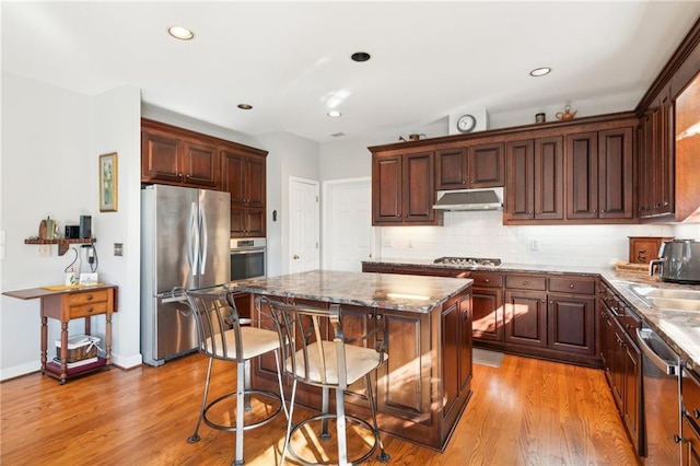 kitchen featuring light stone countertops, a center island, tasteful backsplash, light hardwood / wood-style flooring, and appliances with stainless steel finishes