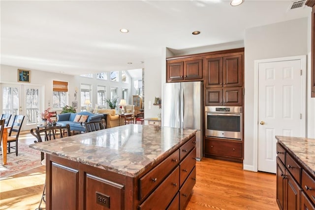 kitchen with french doors, light hardwood / wood-style flooring, a kitchen island, light stone counters, and stainless steel appliances