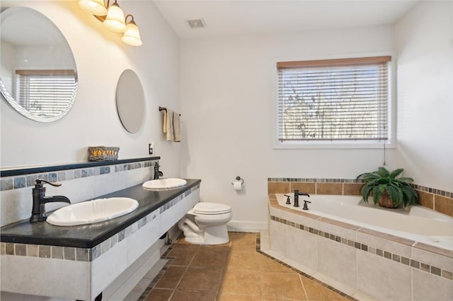 bathroom featuring tile patterned floors, a relaxing tiled tub, toilet, and sink