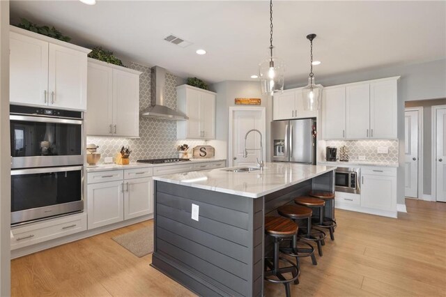 kitchen with appliances with stainless steel finishes, light wood-type flooring, wall chimney range hood, and a sink