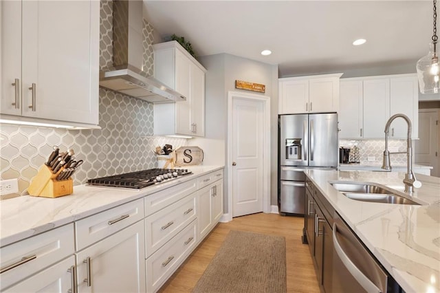 kitchen with light wood-style flooring, stainless steel appliances, white cabinetry, wall chimney exhaust hood, and a sink