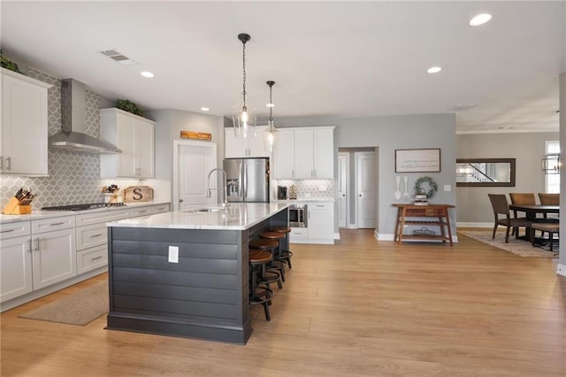 kitchen featuring stainless steel appliances, light wood-style floors, light countertops, and wall chimney range hood