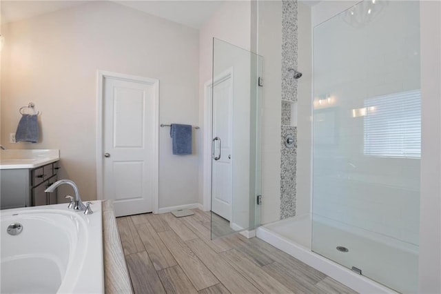 full bath with wood finish floors, tiled shower, baseboards, a bath, and vanity