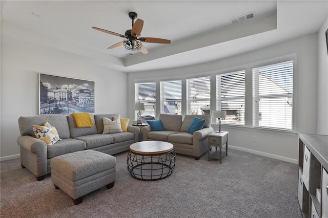 carpeted living area featuring a tray ceiling, baseboards, visible vents, and ceiling fan