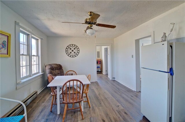 dining area featuring a textured ceiling, baseboards, baseboard heating, and wood finished floors