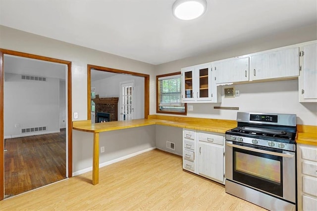 kitchen featuring white cabinets, gas stove, a fireplace, and light hardwood / wood-style floors