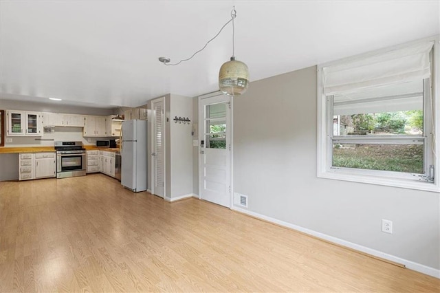 kitchen featuring light wood-type flooring, white cabinets, appliances with stainless steel finishes, and decorative light fixtures