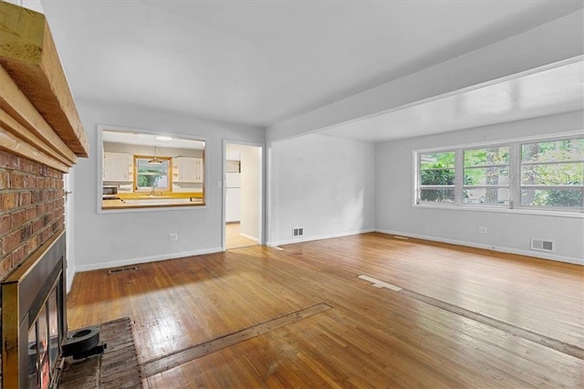 unfurnished living room featuring light hardwood / wood-style flooring and a brick fireplace