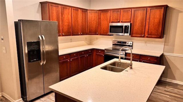 kitchen featuring sink, light hardwood / wood-style floors, stainless steel appliances, light stone countertops, and a center island with sink