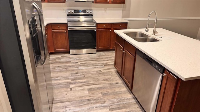 kitchen with appliances with stainless steel finishes, sink, and light hardwood / wood-style flooring