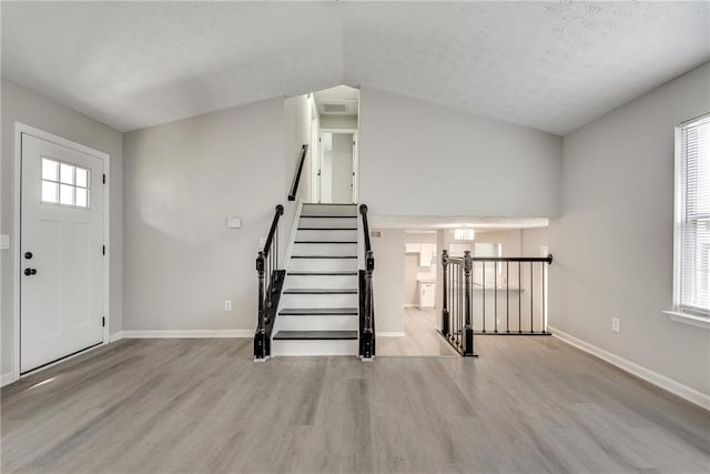 entryway with a textured ceiling, vaulted ceiling, and light wood-type flooring