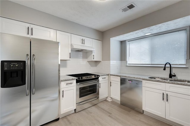 kitchen featuring appliances with stainless steel finishes, light stone counters, white cabinetry, and sink