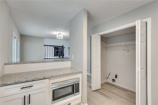 interior space featuring white cabinets, stainless steel microwave, light wood-type flooring, and light stone counters