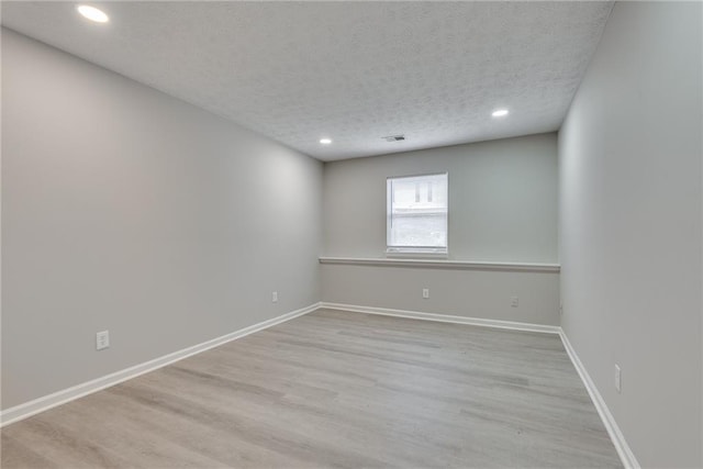 empty room with light wood-type flooring and a textured ceiling